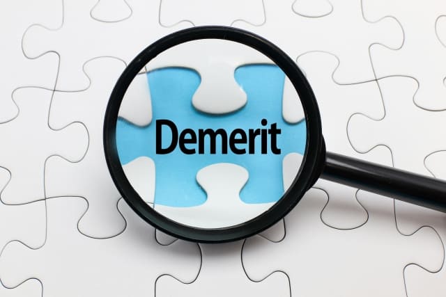 拡大鏡で“Demerit”と書かれたパズルのピースを強調している画像
